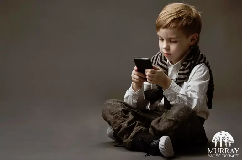 child sitting cross-legged on the floor looking at a mobile device